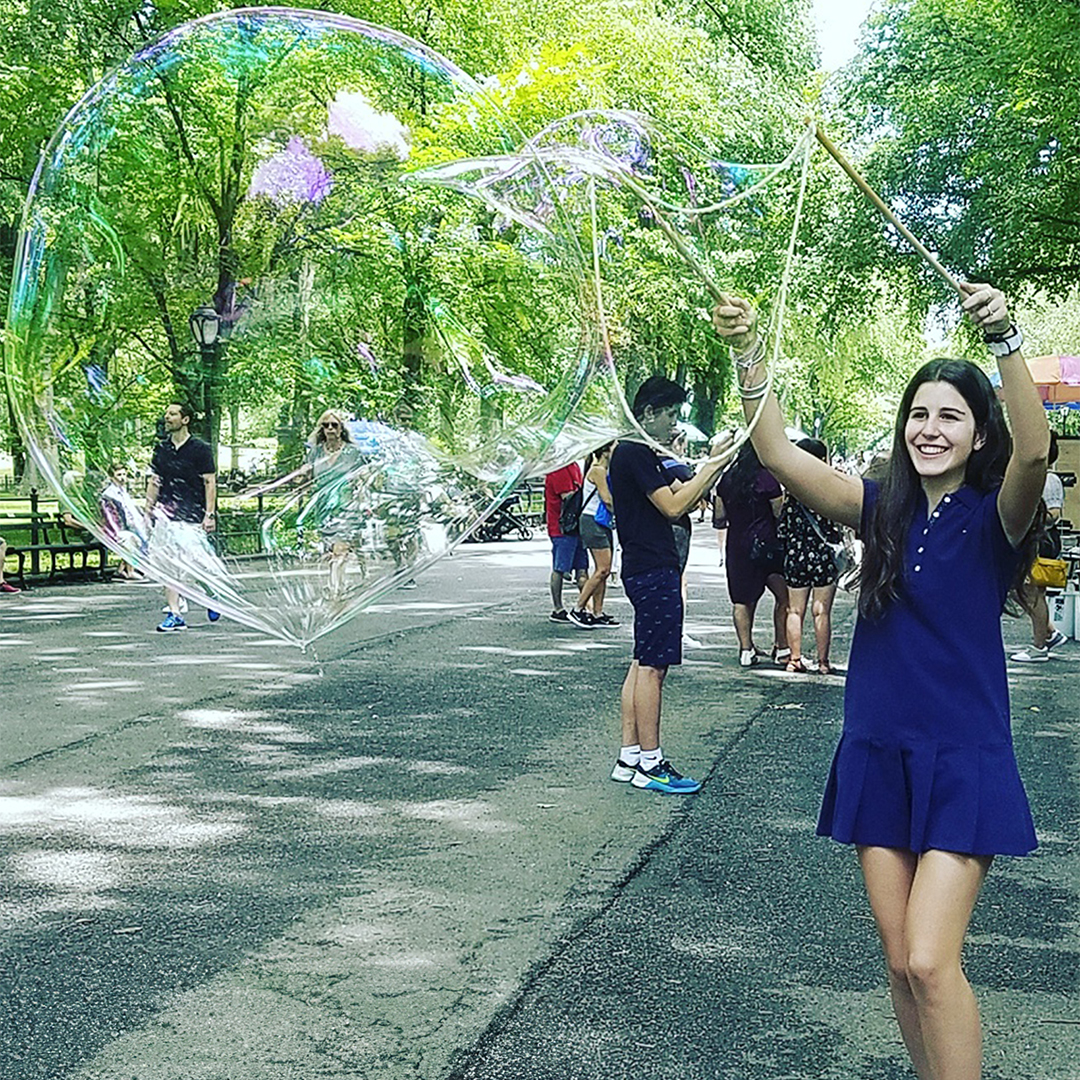 Original photograph of a woman using wooden BubbleStix beneath a giant bubble in the park